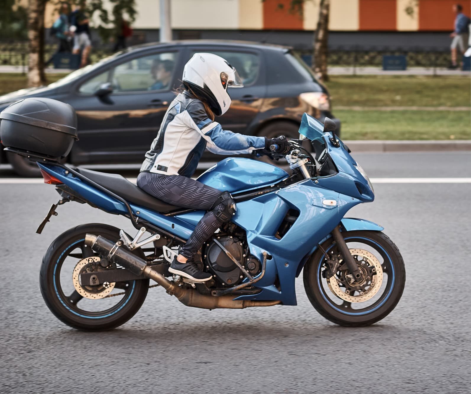 Jeune femme conduisant une moto A2 deux places, avec un casque homologué, des gants homologués et une veste homologuée comportant un air bag